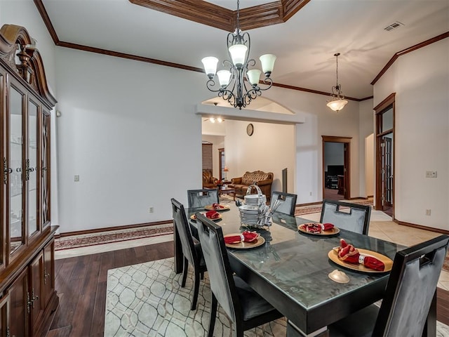 dining area with dark wood-type flooring, ornamental molding, and an inviting chandelier