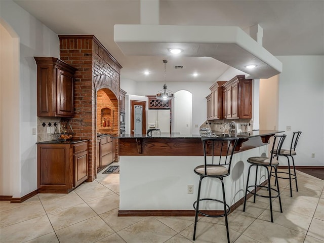 kitchen with pendant lighting, white fridge with ice dispenser, kitchen peninsula, decorative backsplash, and dark stone counters