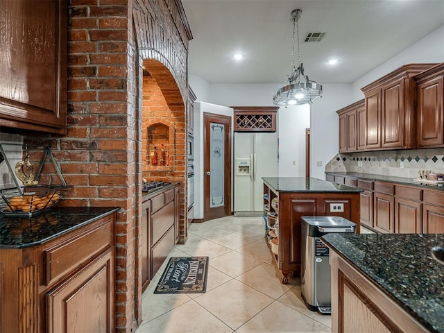 kitchen with dark stone countertops, light tile patterned floors, a kitchen island, white refrigerator with ice dispenser, and decorative backsplash