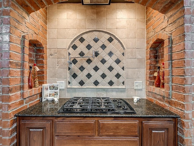 kitchen with tasteful backsplash, brick wall, black gas stovetop, and dark stone countertops