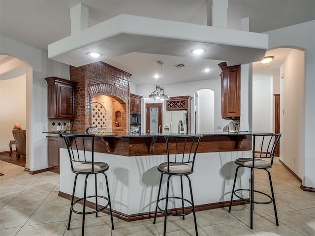 kitchen featuring light tile patterned flooring, a kitchen bar, black microwave, kitchen peninsula, and white fridge with ice dispenser