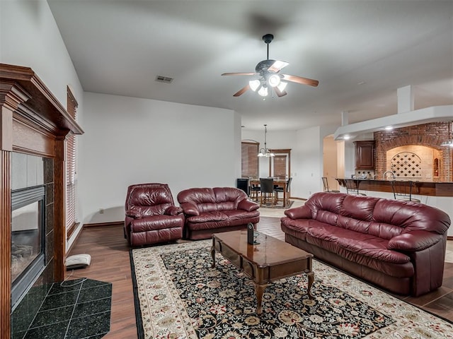 living room featuring ceiling fan, dark hardwood / wood-style flooring, and a tiled fireplace