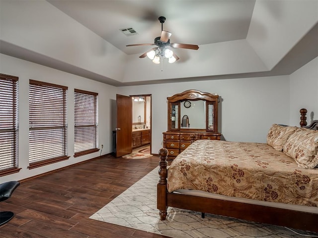 bedroom with ceiling fan, connected bathroom, dark hardwood / wood-style flooring, and a raised ceiling