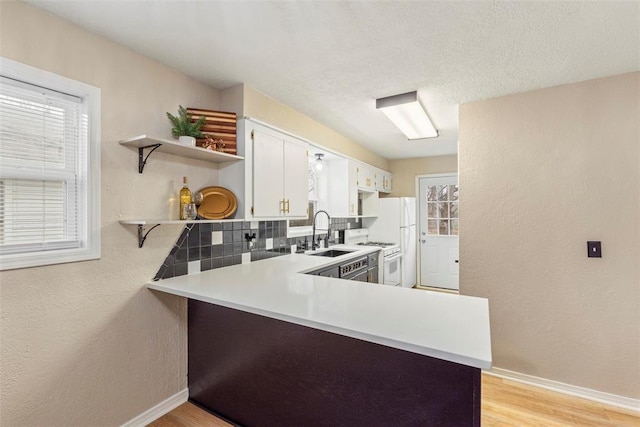 kitchen with sink, backsplash, light hardwood / wood-style floors, white cabinets, and kitchen peninsula