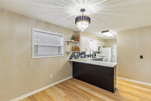 kitchen featuring decorative light fixtures, white cabinetry, sink, kitchen peninsula, and light wood-type flooring