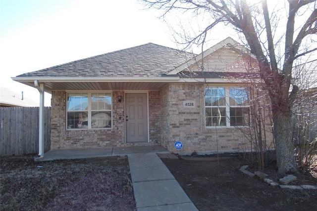 property entrance with fence, brick siding, and roof with shingles