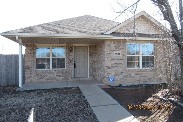 view of front facade featuring a shingled roof and fence