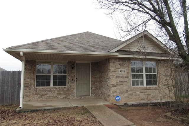 view of front of house featuring fence, brick siding, and a shingled roof