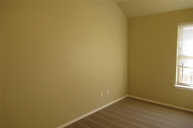 spare room featuring vaulted ceiling, a healthy amount of sunlight, baseboards, and dark colored carpet