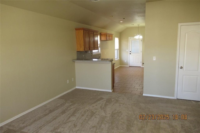 kitchen with brown cabinets, an inviting chandelier, carpet flooring, baseboards, and vaulted ceiling