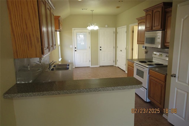 kitchen featuring a sink, a chandelier, a peninsula, white appliances, and dark tile patterned flooring