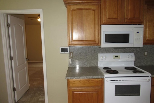 kitchen with tasteful backsplash, white appliances, dark countertops, and baseboards