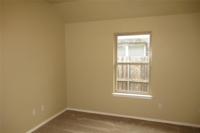 carpeted spare room featuring baseboards and vaulted ceiling