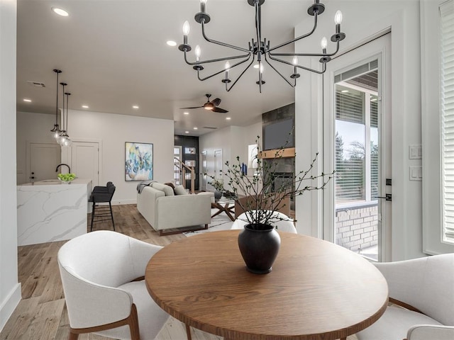 dining area with light hardwood / wood-style flooring, a large fireplace, and ceiling fan