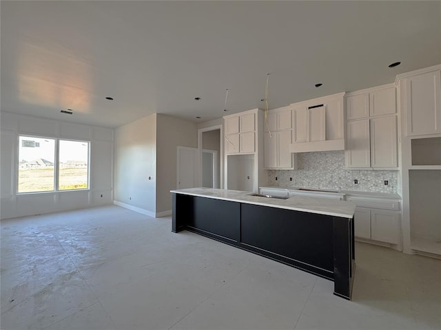 kitchen featuring stovetop, white cabinetry, backsplash, an island with sink, and wall chimney exhaust hood