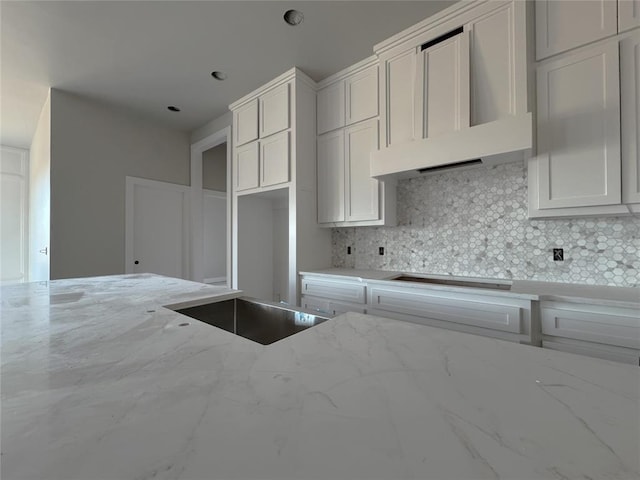 kitchen featuring decorative backsplash, white cabinets, light stone counters, and wall chimney exhaust hood