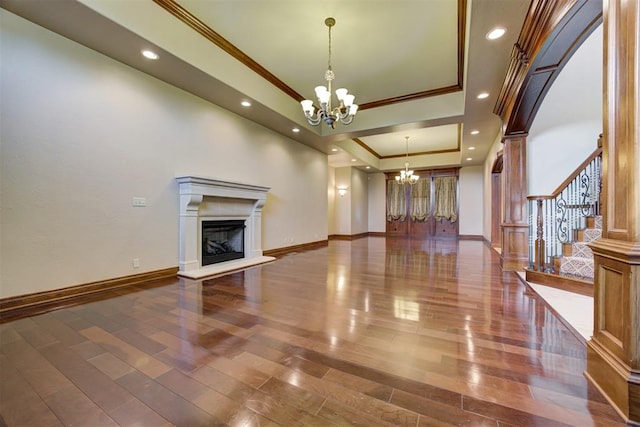 unfurnished living room with a tray ceiling, ornamental molding, a chandelier, and hardwood / wood-style flooring