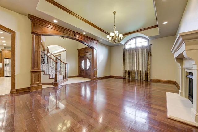 unfurnished living room featuring dark hardwood / wood-style flooring, crown molding, a raised ceiling, and a chandelier