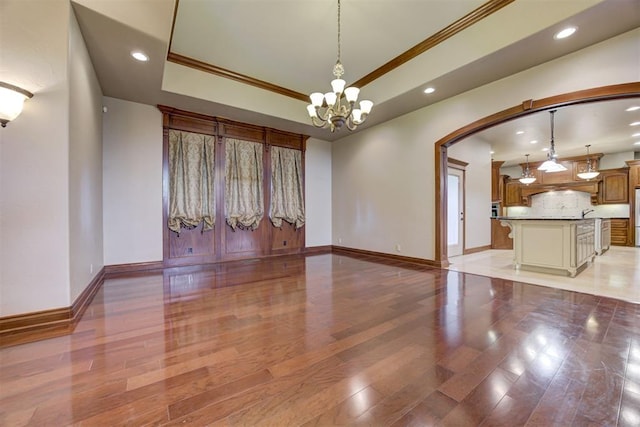 interior space featuring an inviting chandelier, light hardwood / wood-style flooring, ornamental molding, and a raised ceiling