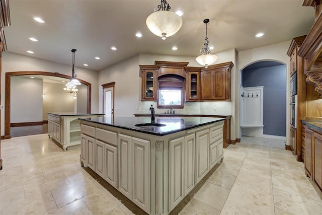 kitchen featuring sink, decorative light fixtures, dark stone counters, and a center island with sink