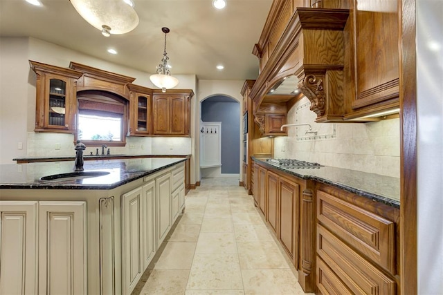 kitchen with stainless steel gas stovetop, sink, dark stone counters, hanging light fixtures, and a kitchen island with sink