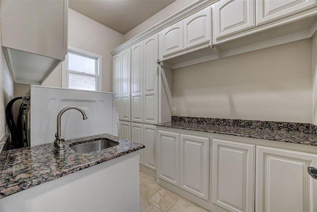 kitchen featuring white cabinetry, dark stone counters, sink, and light tile patterned floors