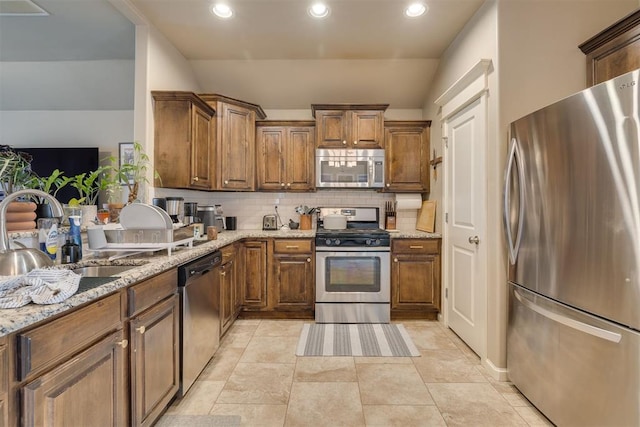 8609 SW 36th Ter, Oklahoma City, OK 73179 - kitchen featuring stainless steel appliances, backsplash, light stone countertops, brown cabinetry, and recessed lighting