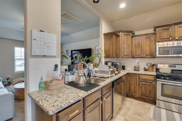 8609 SW 36th Ter, Oklahoma City, OK 73179 - kitchen featuring stainless steel appliances, decorative backsplash, light stone countertops, vaulted ceiling, and brown cabinetry