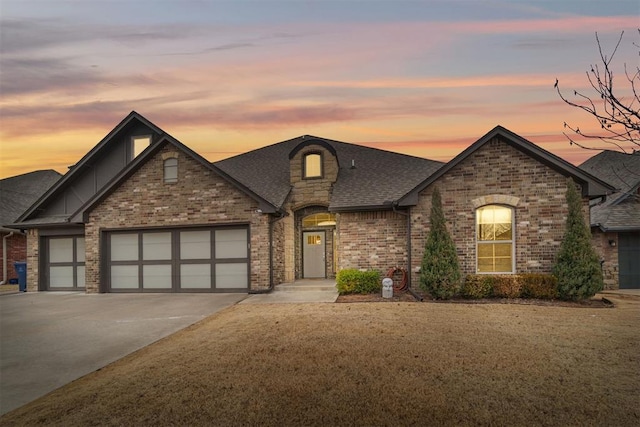 view of front of home with concrete driveway, brick siding, an attached garage, and roof with shingles