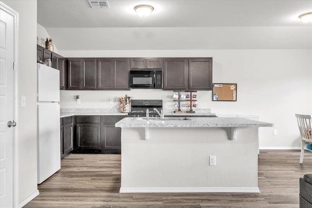 kitchen with a breakfast bar area, an island with sink, white fridge, and stove