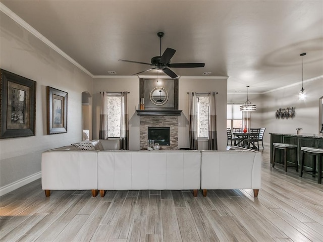 living room with crown molding, a wealth of natural light, light hardwood / wood-style floors, and a stone fireplace