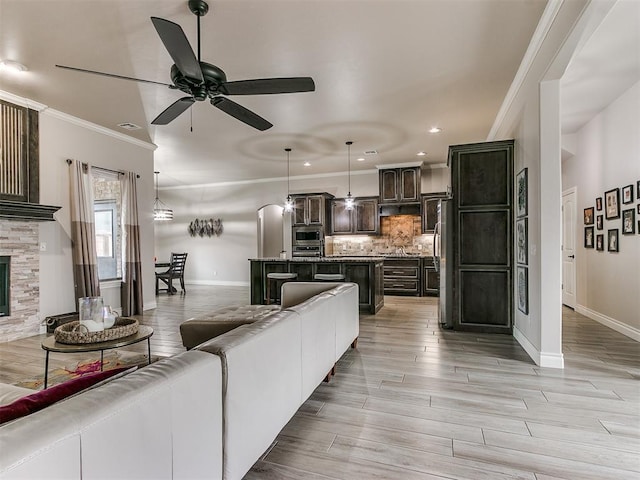 living room featuring a stone fireplace, ornamental molding, ceiling fan, and light wood-type flooring