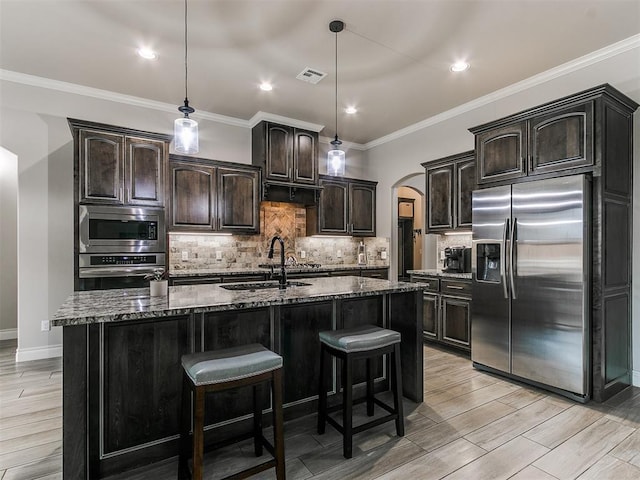 kitchen featuring stainless steel appliances, a kitchen island with sink, pendant lighting, and dark stone counters