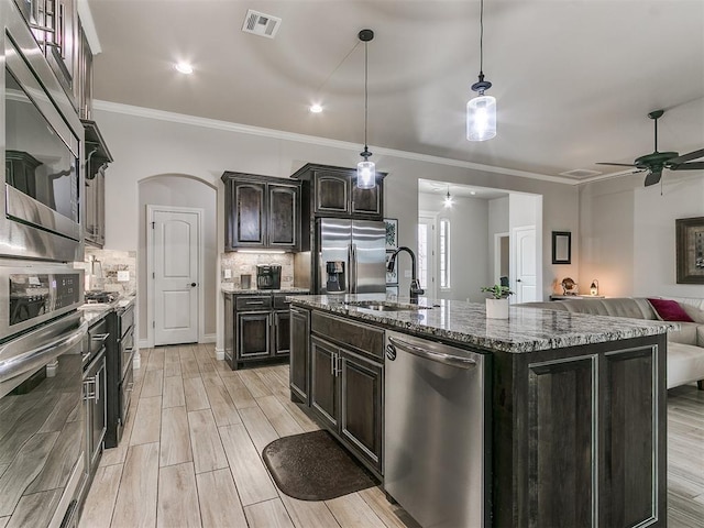 kitchen featuring pendant lighting, sink, appliances with stainless steel finishes, dark brown cabinets, and an island with sink