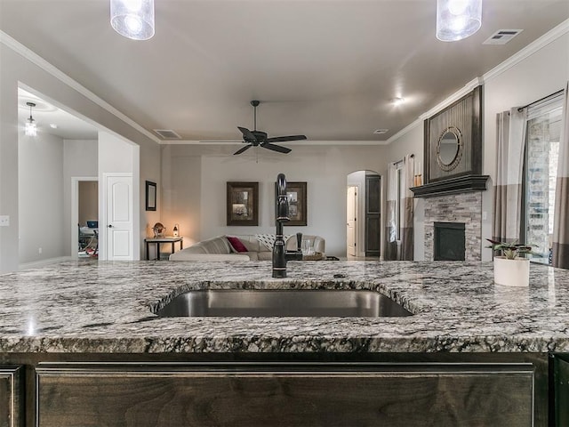 kitchen featuring stone counters, a stone fireplace, sink, ornamental molding, and ceiling fan