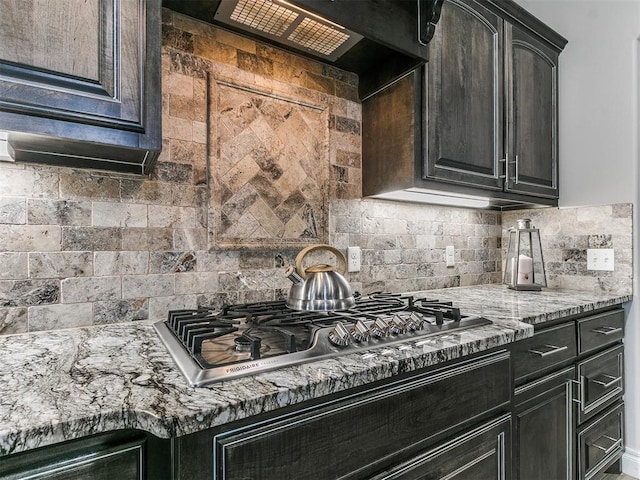 kitchen featuring stainless steel gas stovetop, extractor fan, light stone countertops, and decorative backsplash