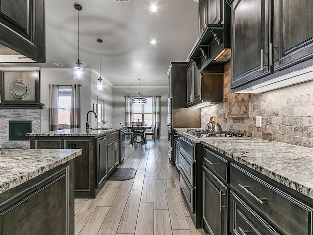 kitchen featuring sink, light stone counters, decorative light fixtures, a kitchen island with sink, and decorative backsplash