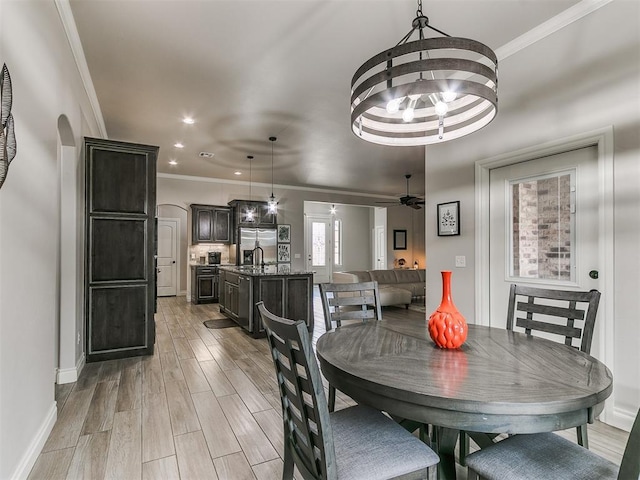 dining area featuring crown molding, sink, ceiling fan with notable chandelier, and light hardwood / wood-style floors