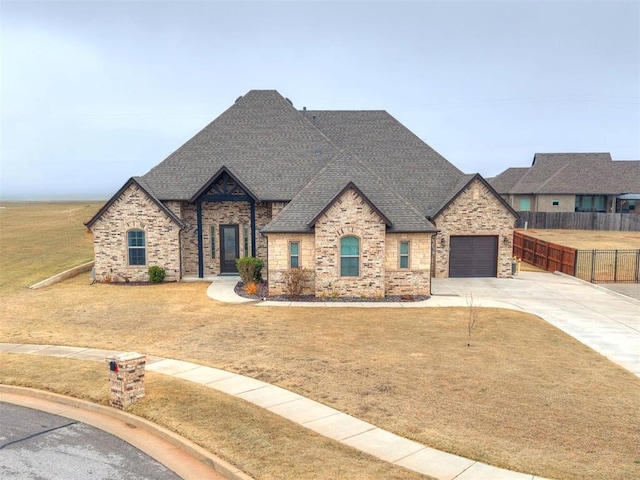 french provincial home with concrete driveway, roof with shingles, a front yard, and fence