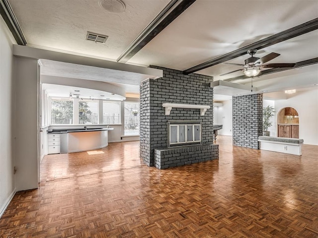 unfurnished living room featuring ceiling fan, a fireplace, a textured ceiling, parquet flooring, and beamed ceiling