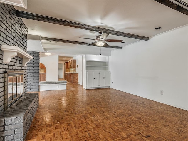 unfurnished living room with ceiling fan, dark parquet flooring, a fireplace, and beamed ceiling