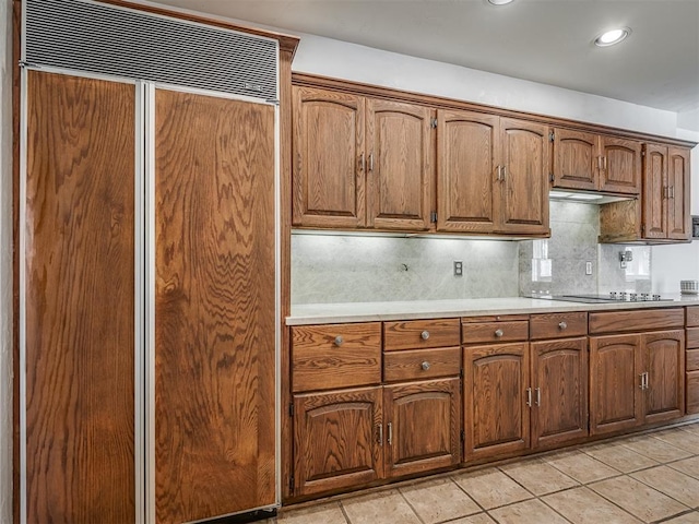 kitchen featuring black electric stovetop, paneled built in fridge, light tile patterned floors, and decorative backsplash