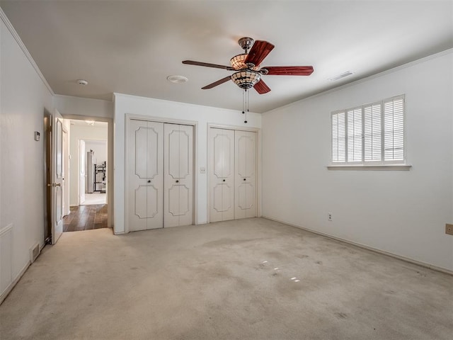 unfurnished bedroom with multiple closets, ceiling fan, carpet flooring, and crown molding