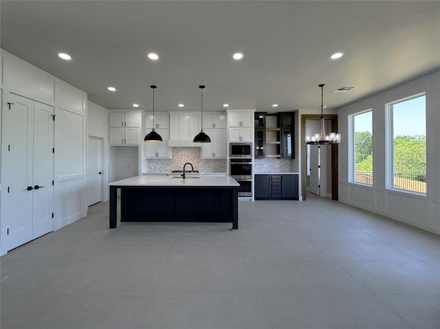 15521 Aparados Way, Edmond, OK 73013 - kitchen featuring visible vents, a sink, stainless steel microwave, decorative backsplash, and a notable chandelier