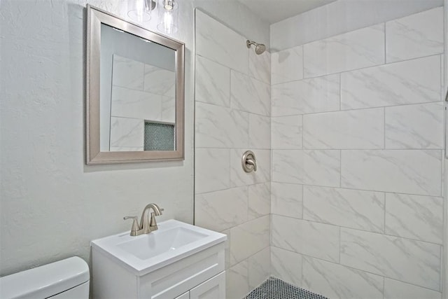 bathroom featuring vanity, toilet, and a tile shower