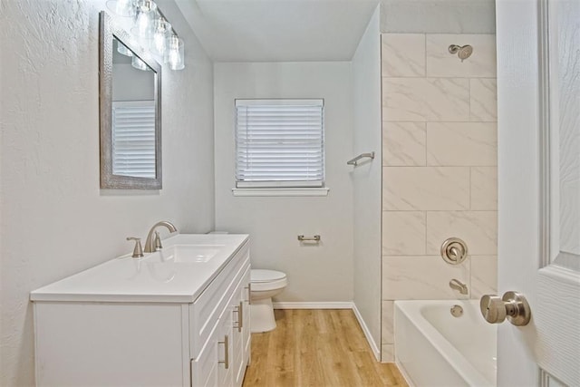 full bathroom with hardwood / wood-style flooring, vanity, tiled shower / bath, and toilet