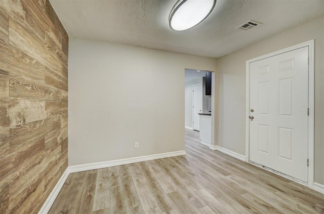 spare room featuring a textured ceiling, light wood-type flooring, and wood walls