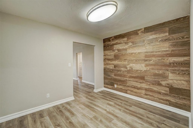 empty room with a textured ceiling, wooden walls, and light hardwood / wood-style floors