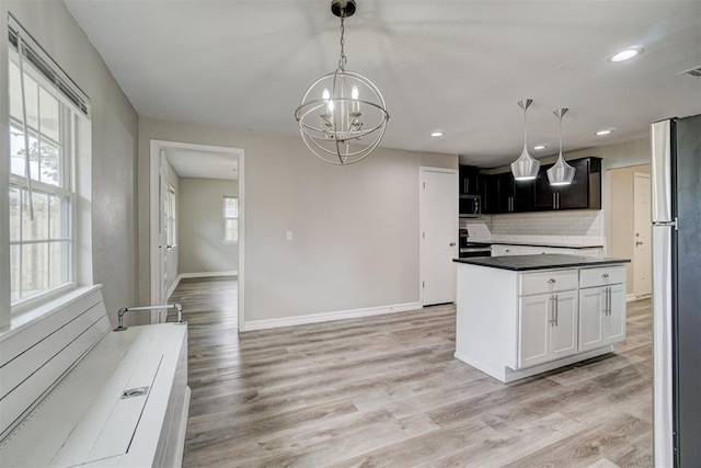 kitchen featuring appliances with stainless steel finishes, pendant lighting, decorative backsplash, a notable chandelier, and light wood-type flooring