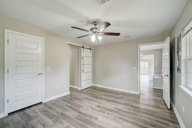 unfurnished bedroom with ceiling fan, a barn door, and light hardwood / wood-style floors